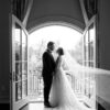 A bride and groom share an intimate moment in front of elegant French doors, captured in black and white by one of the best wedding photographers 2025.