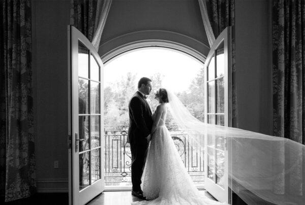 A bride and groom share an intimate moment in front of elegant French doors, captured in black and white by one of the best wedding photographers 2025.