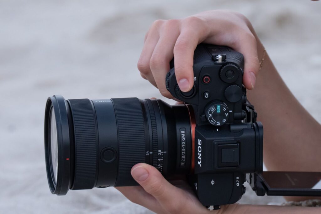 Close-up of hands holding the Sony A7 V camera with a 24–70mm G Master II lens, adjusting settings while shooting outdoors.