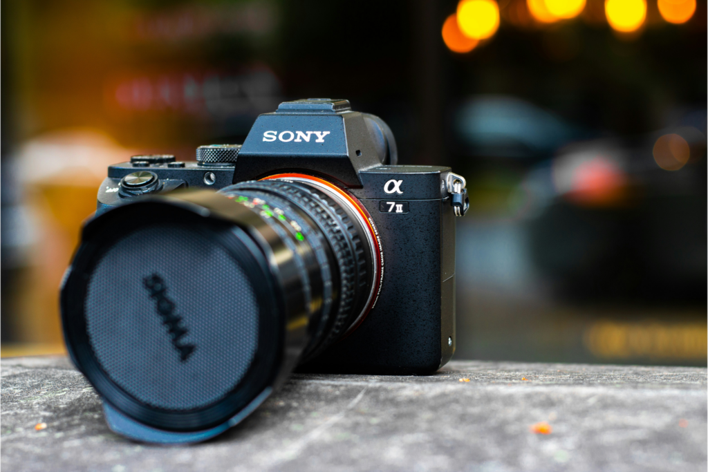 Sony Alpha A7 II mirrorless camera with Sigma lens on a stone surface with bokeh city lights — part of the A7 lineage among cameras that were ugly when they launched