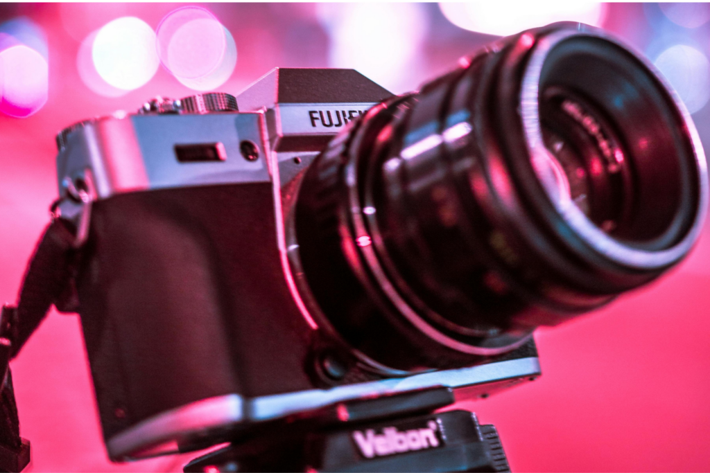 Fujifilm X-T mirrorless camera on a Velbon tripod against neon city bokeh at night — one of the cameras that were ugly when they launched before becoming collector favorites