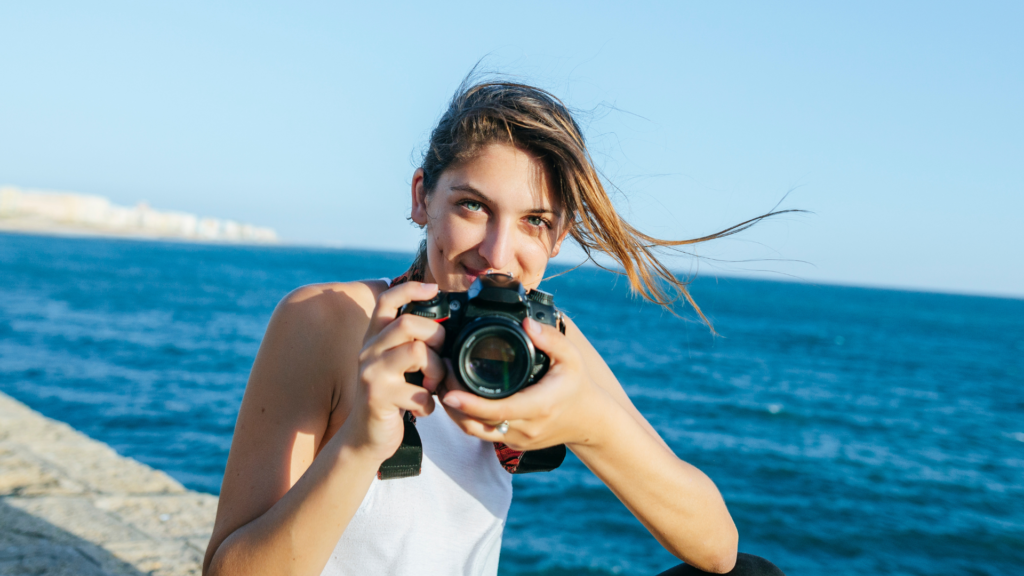 A young photographer holds a DSLR camera outdoors by the sea — where is photography's money actually going in 2026?