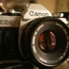 Close-up of Canon AE-1 film camera with FD 50mm f/1.8 lens on wooden surface — the camera that defined photography is turning 50