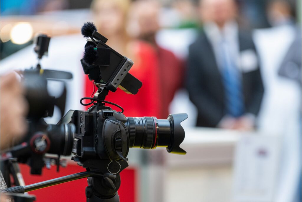 Broadcast camera on tripod at a red carpet press event with blurred journalists and guests in the background