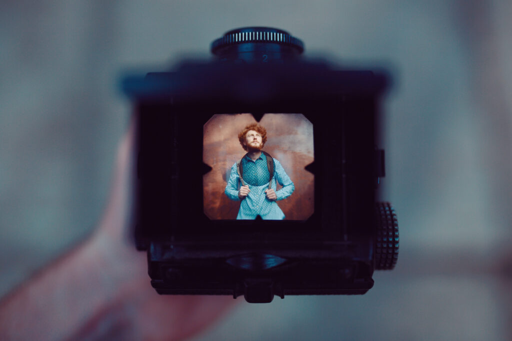 Photographer framing a portrait through the viewfinder of a vintage medium format camera — a reminder that human perspective is at the heart of photography, regardless of whether AI is killing photography
