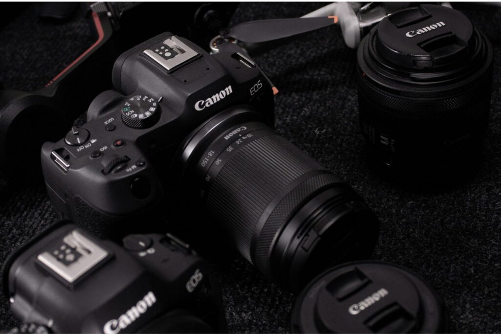 Canon EOS mirrorless used camera with 18-150mm kit lens surrounded by additional Canon lenses and gear on a dark surface