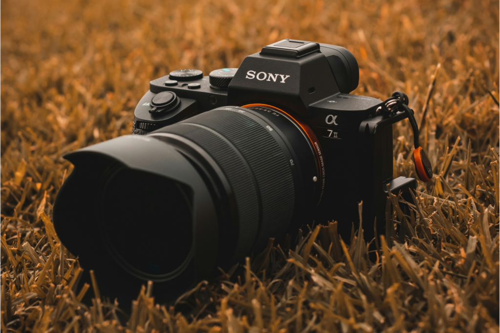 Sony A7 II mirrorless camera with zoom lens resting in dry grass — does camera gear matter for real-world shooting conditions