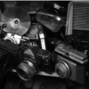 Camera Companies Make Cameras Nobody Wants — pile of discarded vintage film cameras, flash bulbs, and obsolete gear.