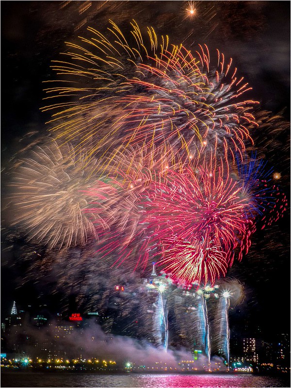 Fireworks photography — dense red, gold, and blue bursts reflected over the New York City waterfront during the Macy's Fourth of July show.