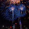 How to photograph fireworks — blue and gold long-exposure bursts arcing over the New York City skyline at night.