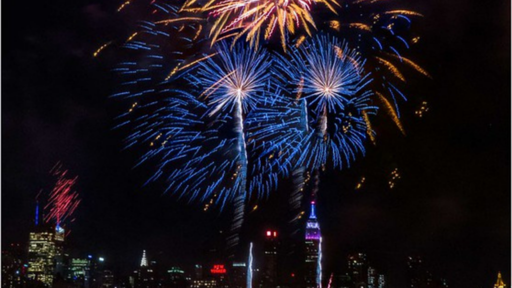 How to photograph fireworks — blue and gold long-exposure bursts arcing over the New York City skyline at night.