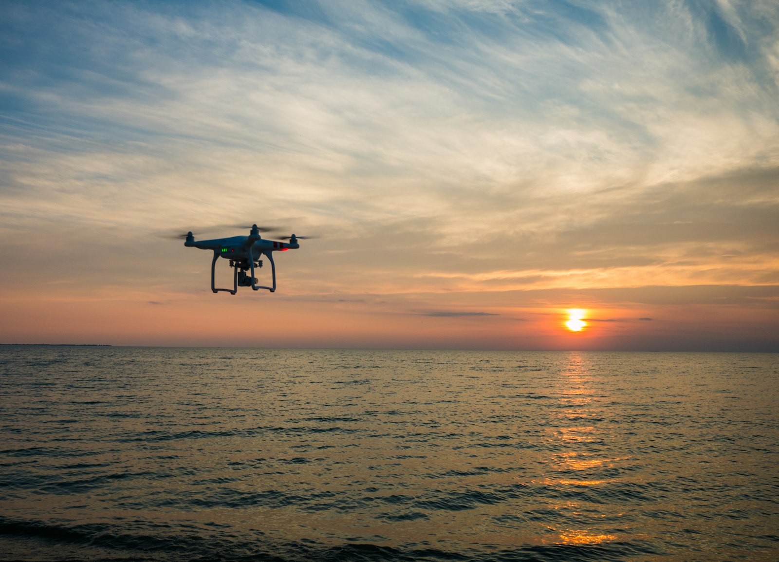 quadcopter drone flying over water at sunset