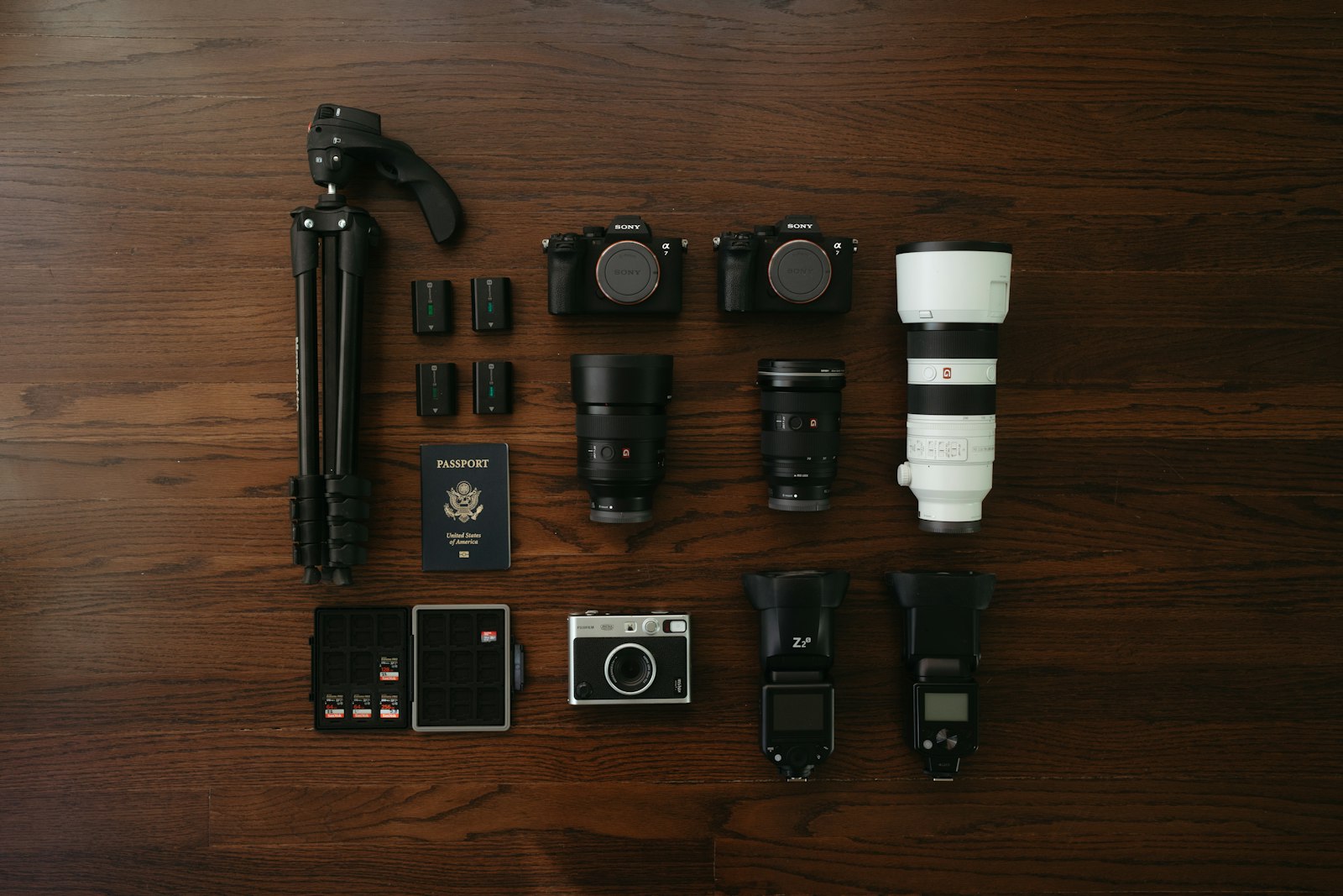 top-down view of two black mirrorless camera bodies with lenses, tripod, and accessories arranged on a wooden surface