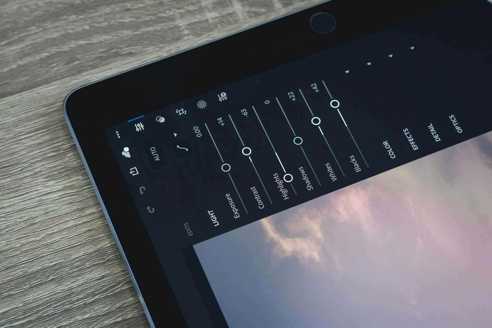 close-up of a tablet screen showing photo editing adjustment sliders over a sky image