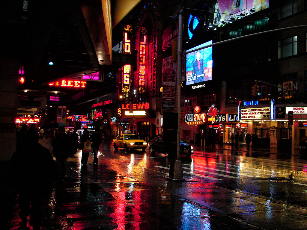 neon-lit city street at night with taxis and colorful sign reflections on wet pavement