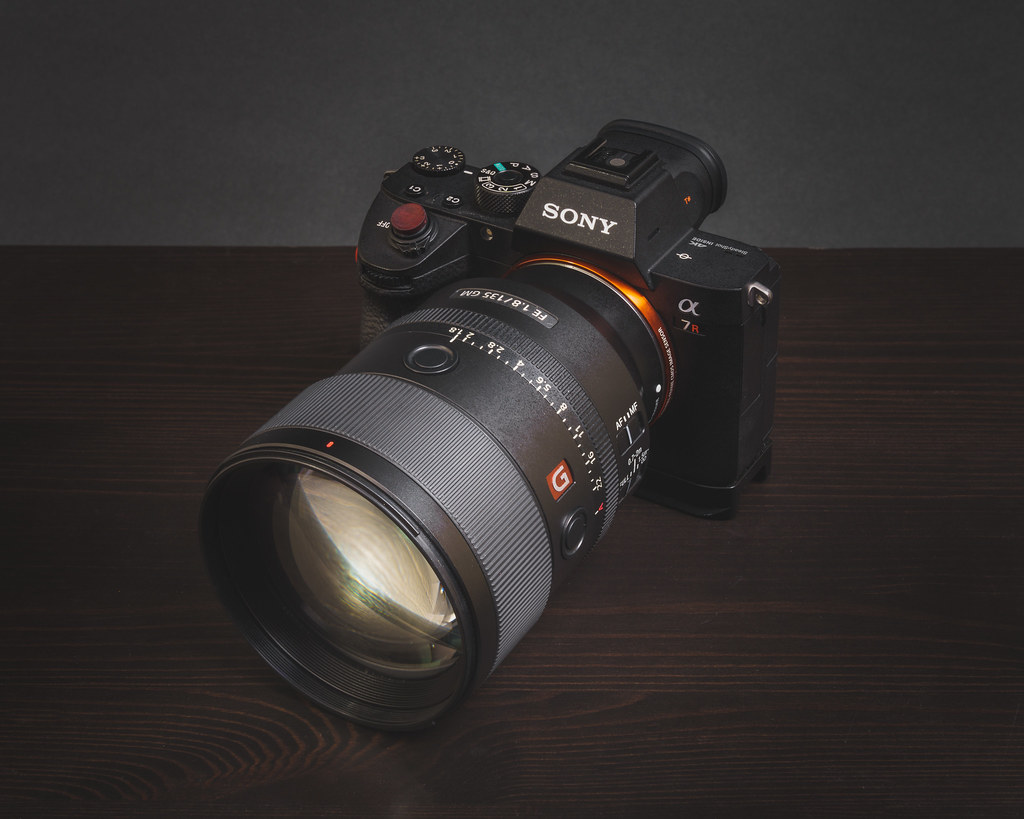 Sony mirrorless camera with a 135mm telephoto lens mounted, on a dark wooden surface under soft studio lighting