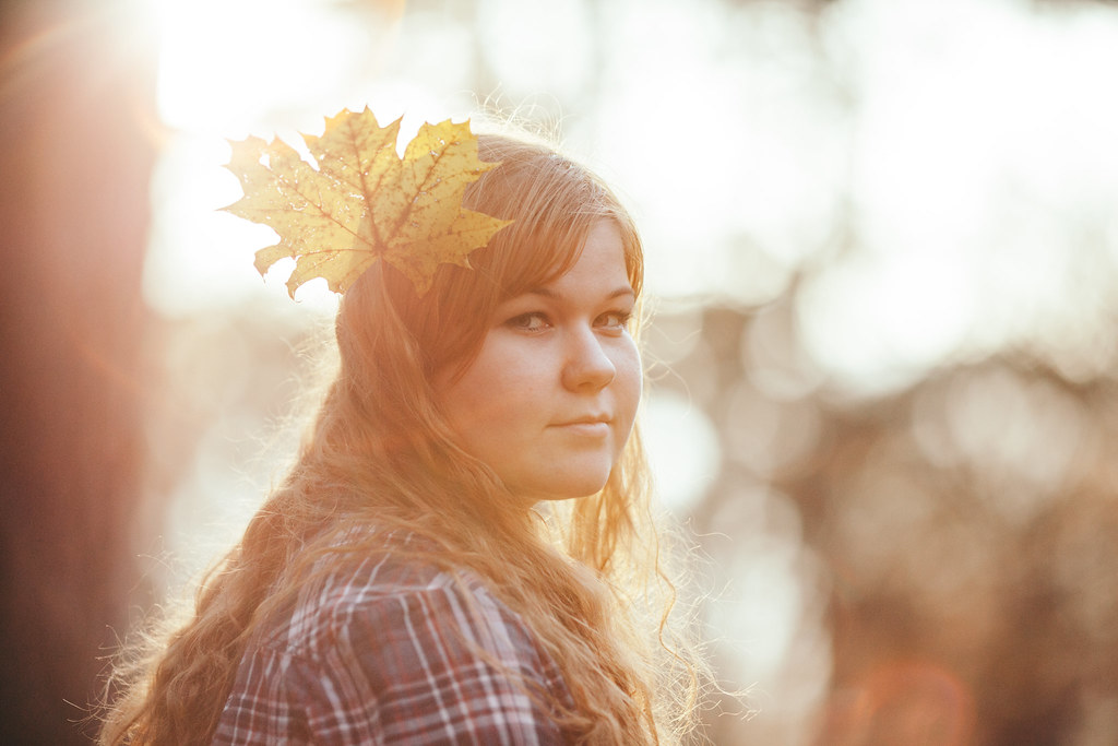backlit portrait of a woman with a maple leaf in her hair at golden hour with warm tones and soft bokeh