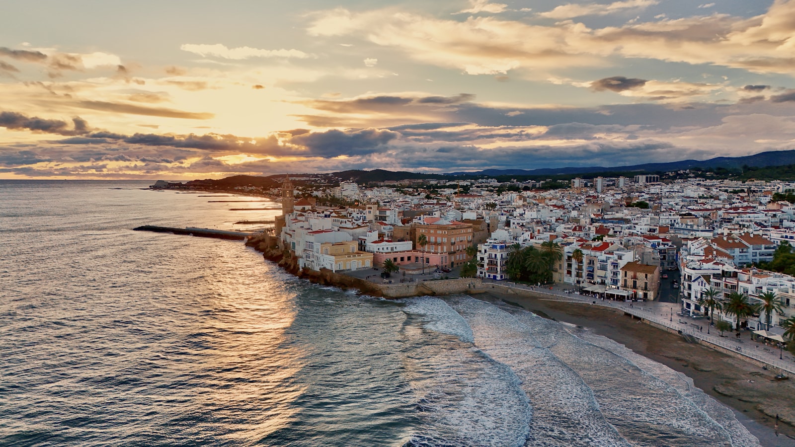 aerial view of a coastal town and beach at sunset with waves along the shore