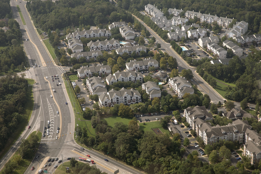 aerial view of a suburban residential development showing rooftops, parking lots, and a roadway
