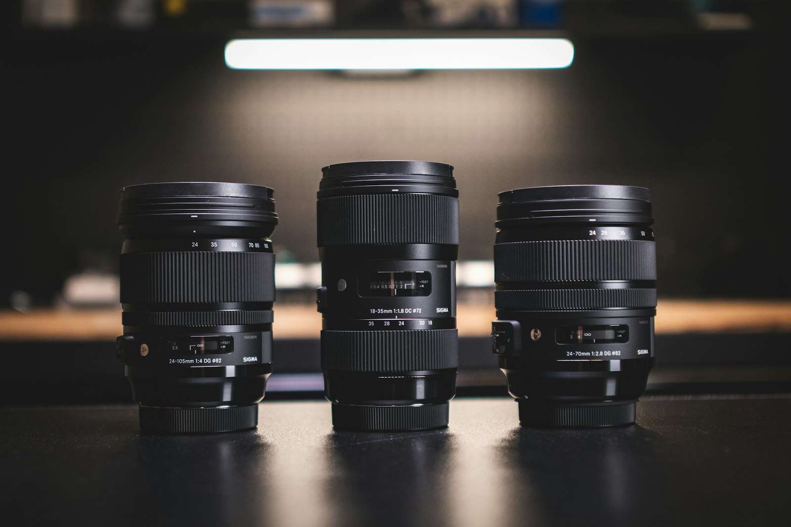 three black camera lenses standing side by side on a dark table