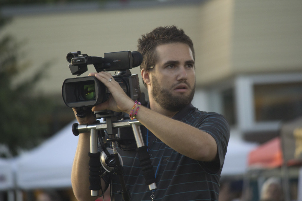 man operating a professional video camera mounted on a tripod rig at an outdoor event
