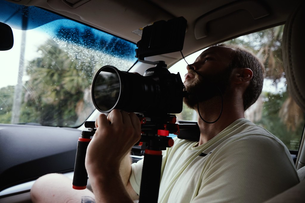 videographer operating a handheld-rigged cinema camera inside a vehicle on location