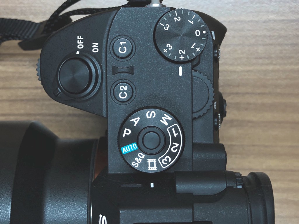 close-up of top control dials on a black mirrorless camera body on a wooden surface