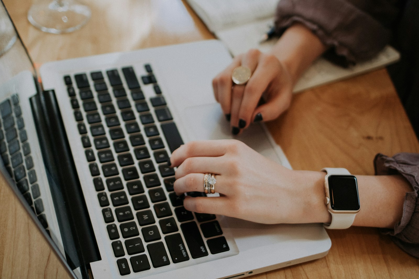 close-up of hands typing on a MacBook laptop at a wooden desk