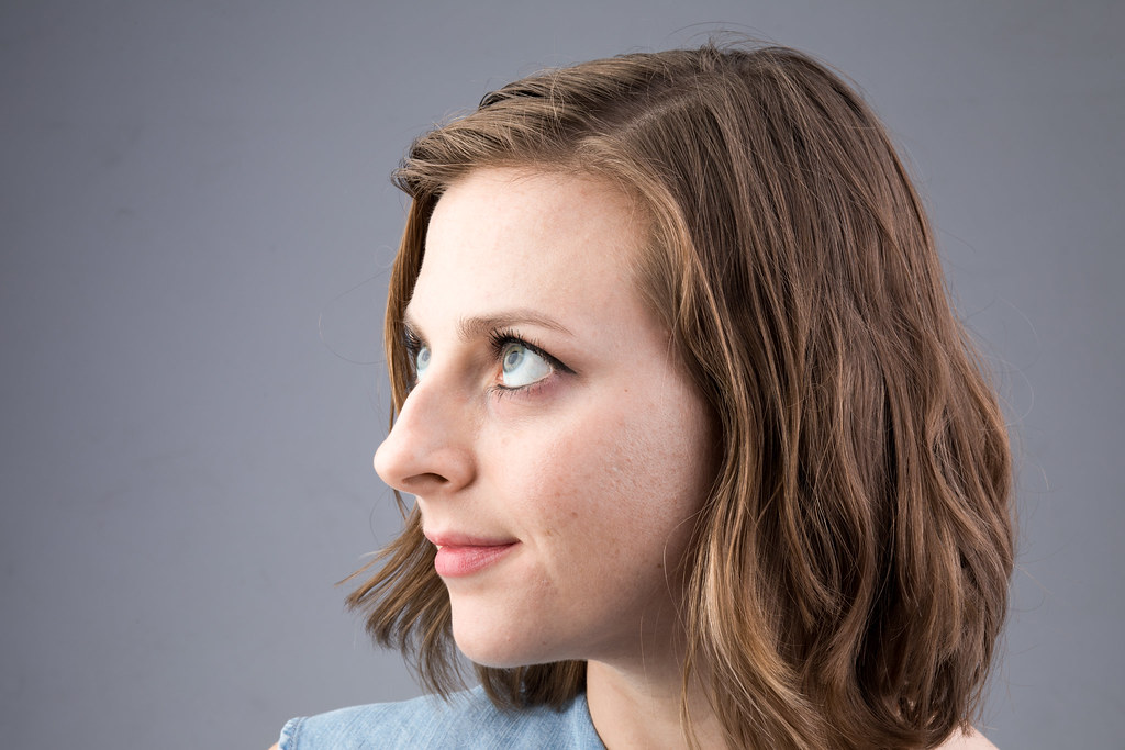 profile studio portrait of a woman with wavy brown hair against a gray backdrop under soft lighting
