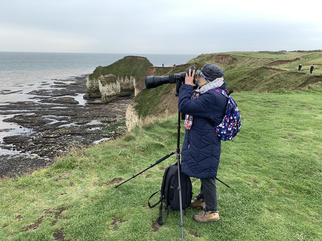 photographer using a camera with telephoto lens on a tripod at a coastal cliff location