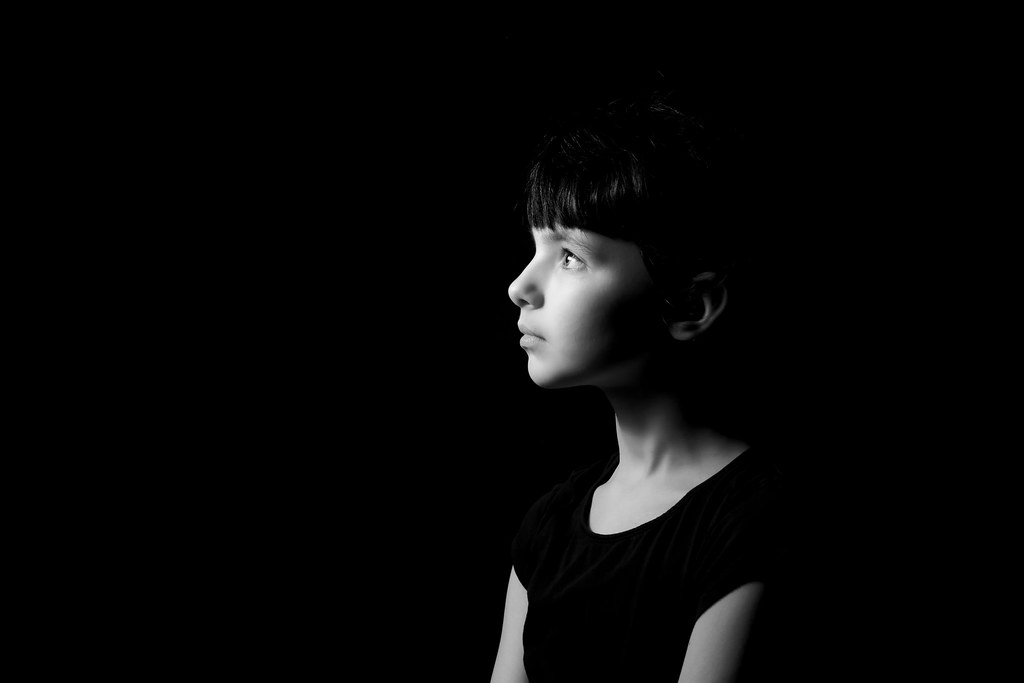 black and white studio profile portrait of a young model against a dark background with directional lighting
