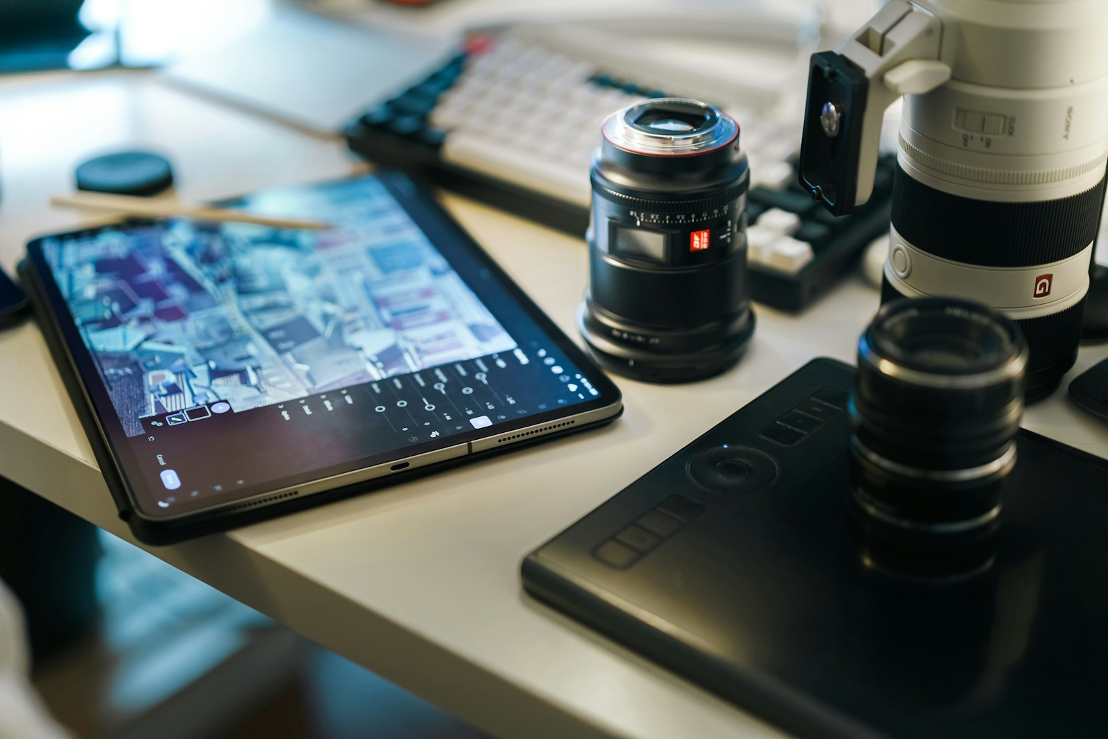 tablet showing photos on a desk beside camera lenses and a graphics tablet