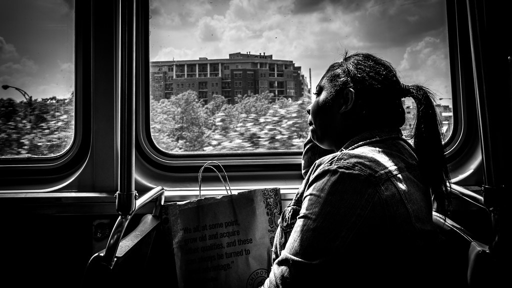 black and white portrait of a woman seated by a bus window with light falling across her face