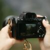 hands holding a mirrorless camera at eye level framing a landscape outdoors