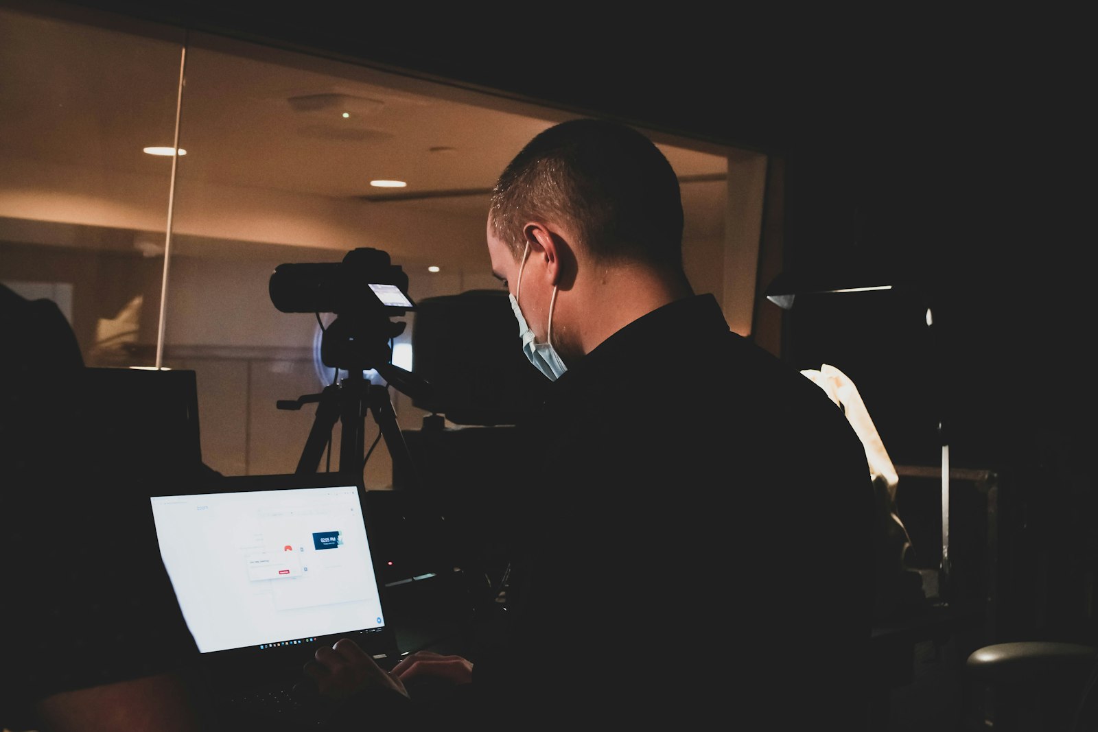 person working on a laptop beside a camera on a tripod in a dark room