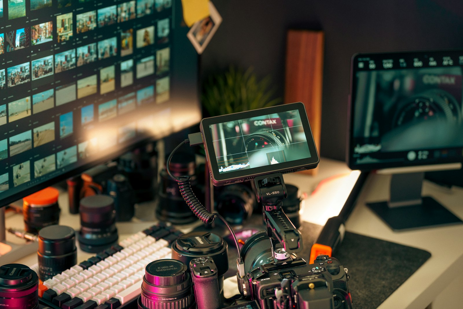 camera and lenses on a desk beside monitors displaying video clips in an editing setup