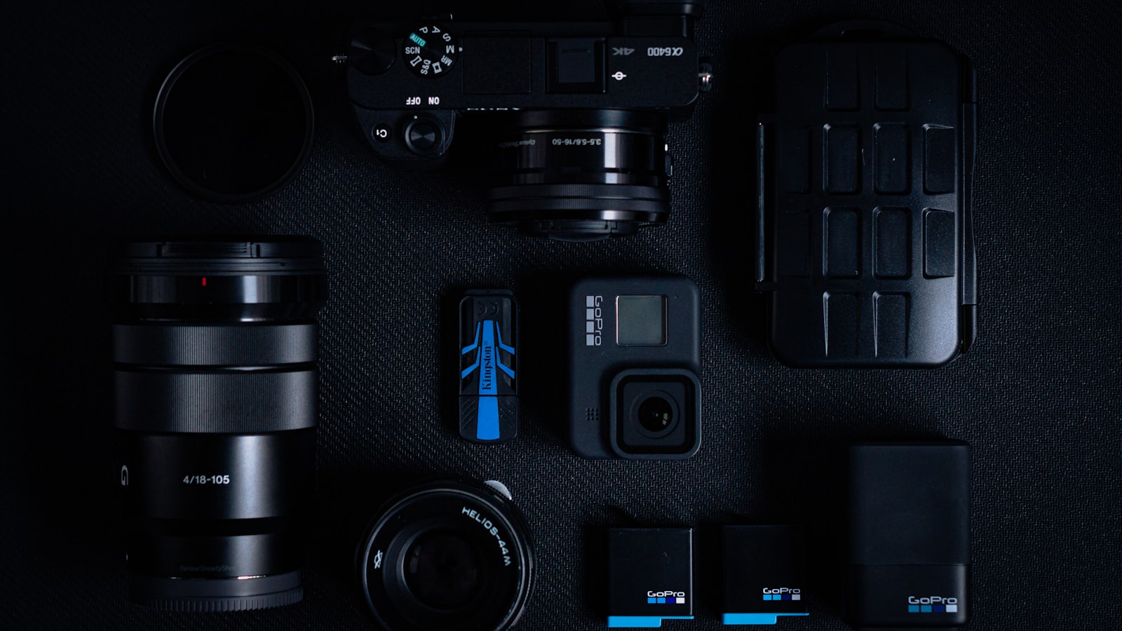 action camera surrounded by lenses, batteries, and accessories arranged on a dark flat surface
