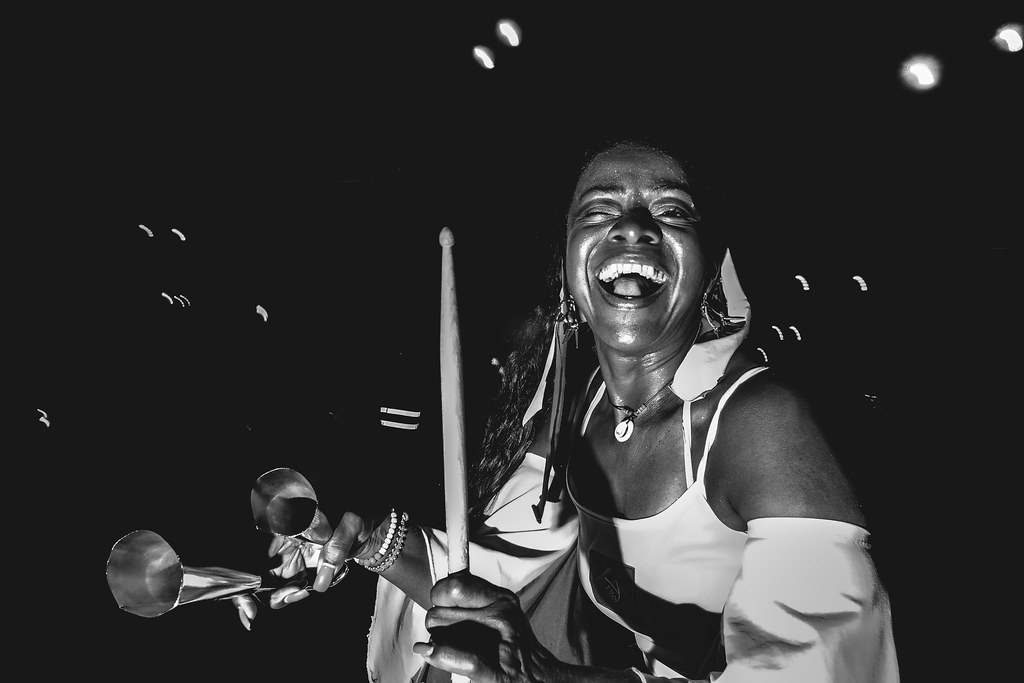 black and white night portrait of a laughing woman holding drumsticks against a dark background with light bokeh
