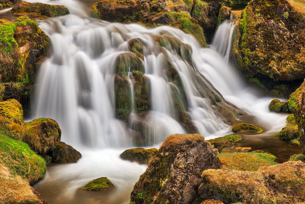 long-exposure cascade flowing over moss-covered boulders in soft light