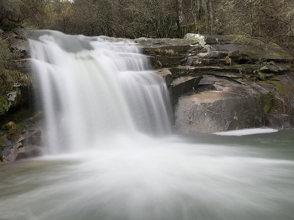long exposure waterfall with silky white water cascading over dark rock into a pool in a forest