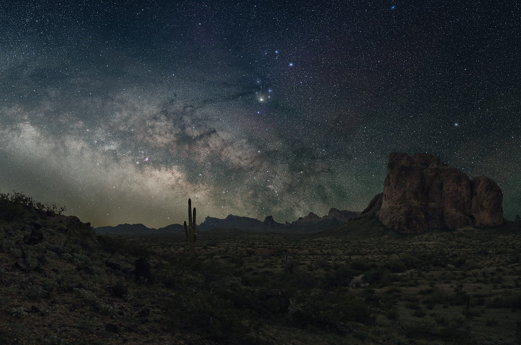 Milky Way arching over silhouetted desert hills and rock formations at night