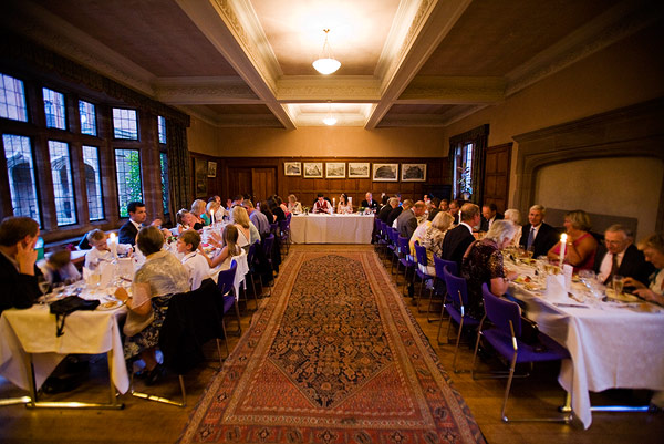 wide-angle interior view of a wedding reception with seated guests at long tables in a wood-paneled hall