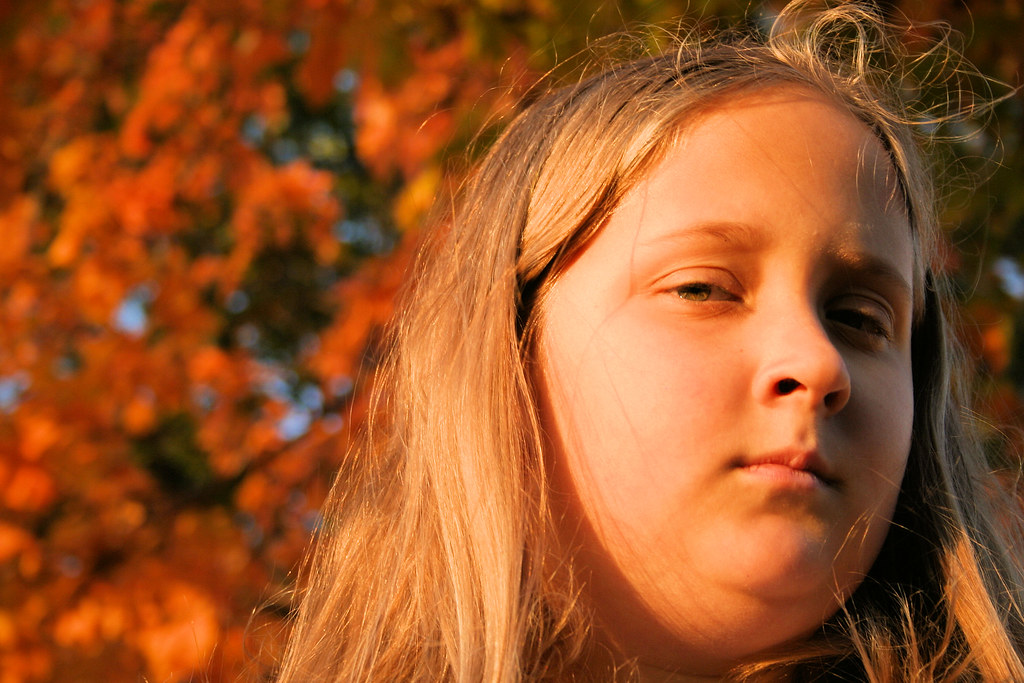 young girl photographed outdoors in warm golden light with orange autumn leaves in the background