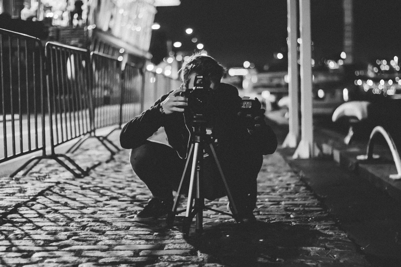 photographer crouching with a DSLR camera on a tripod on a city street at night