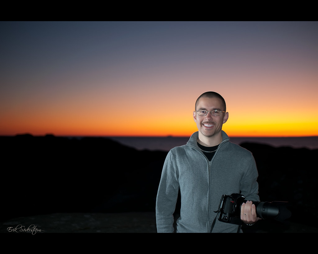 photographer holding a DSLR camera outdoors against an orange dusk sky