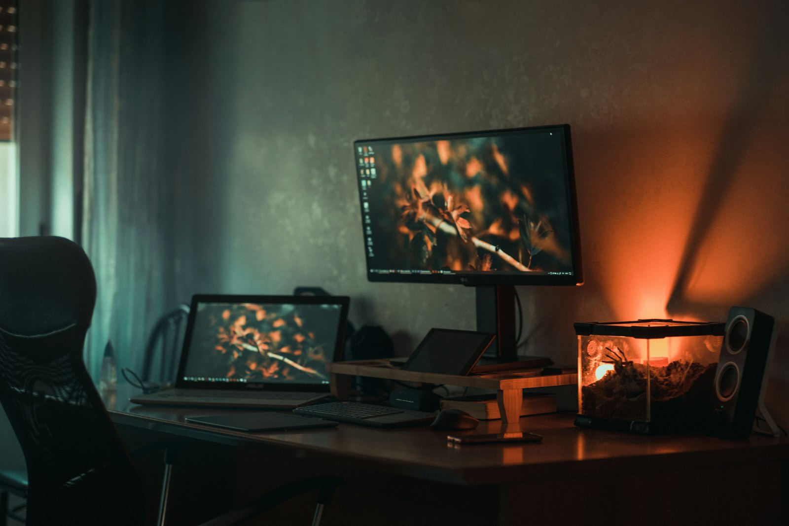 large desktop monitor and laptop on a wooden desk in a dimly lit room at night