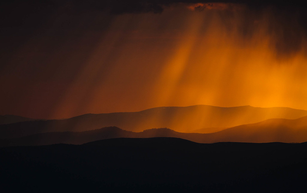 landscape of mountain silhouettes with dramatic orange light rays breaking through clouds at sunset