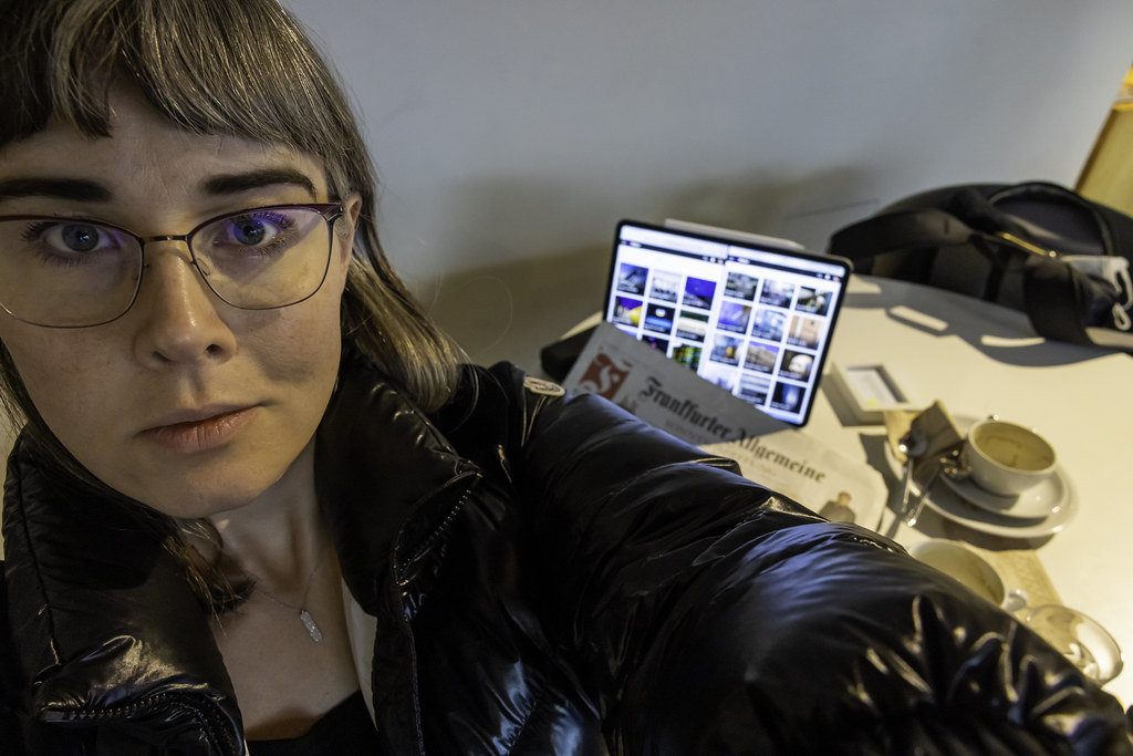 person in a black jacket with a tablet displaying a photo gallery on a table with coffee and newspaper