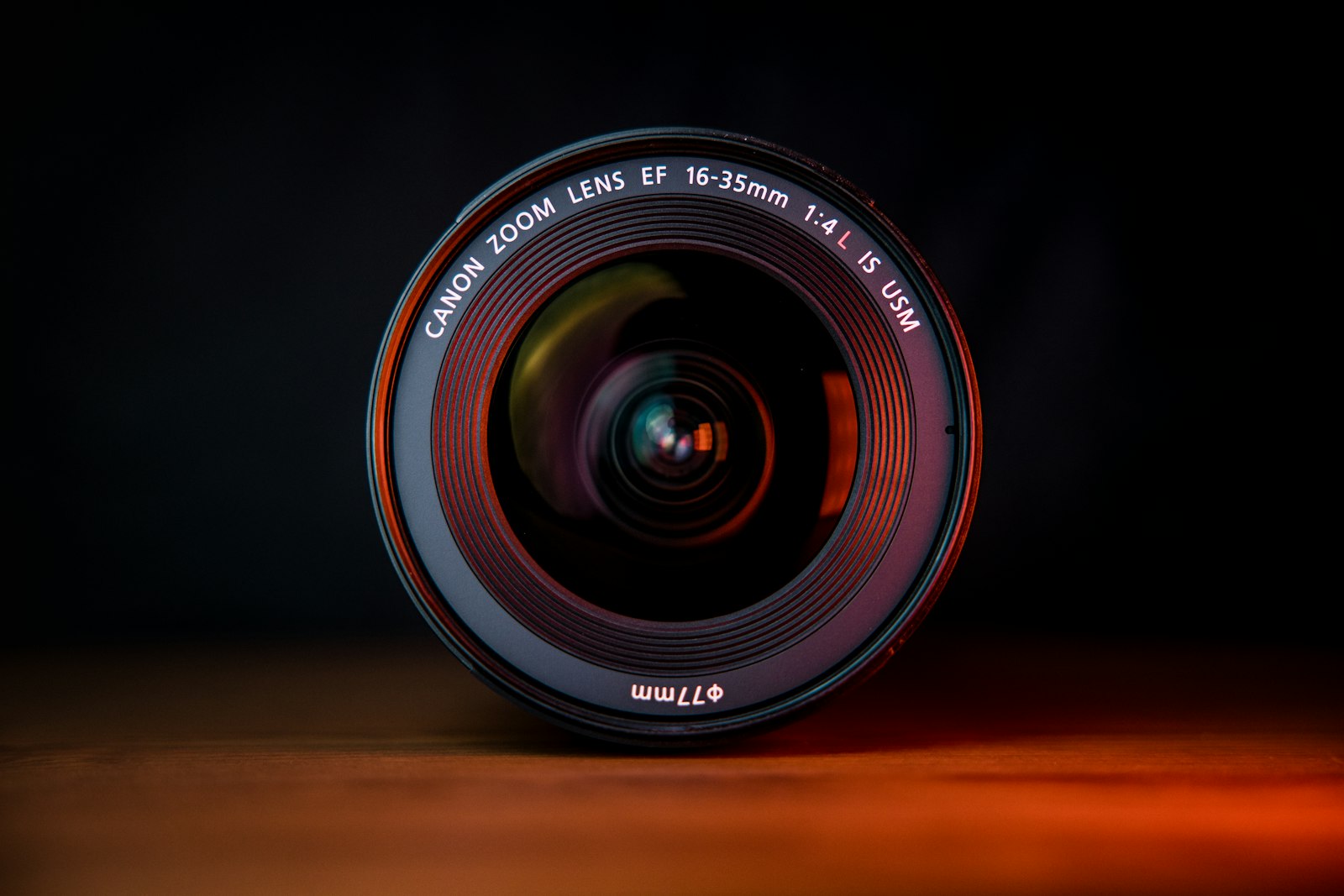 Canon EF 16-35mm zoom lens standing on a wooden table against a dark background
