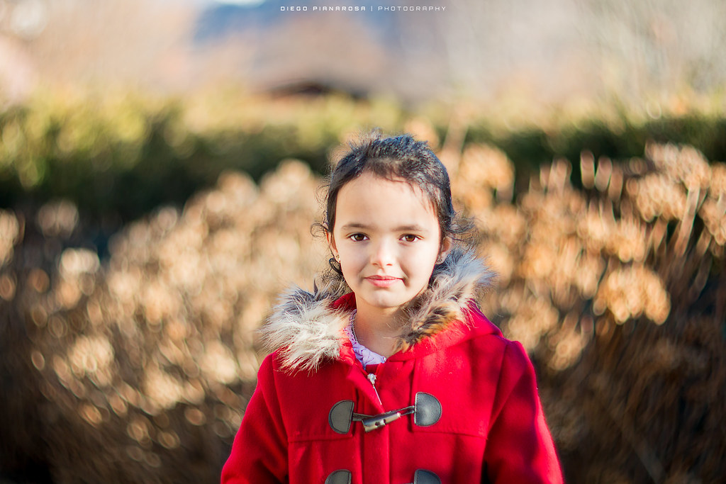 young girl in a red coat standing in front of a swirly golden bokeh background outdoors